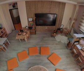 Ahşap raflar, alçak masalar ve turuncu yer minderleri bulunan sınıf