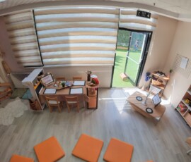 Panjurlu pencere önünde ahşap oyun mobilyaları ve turuncu minderler